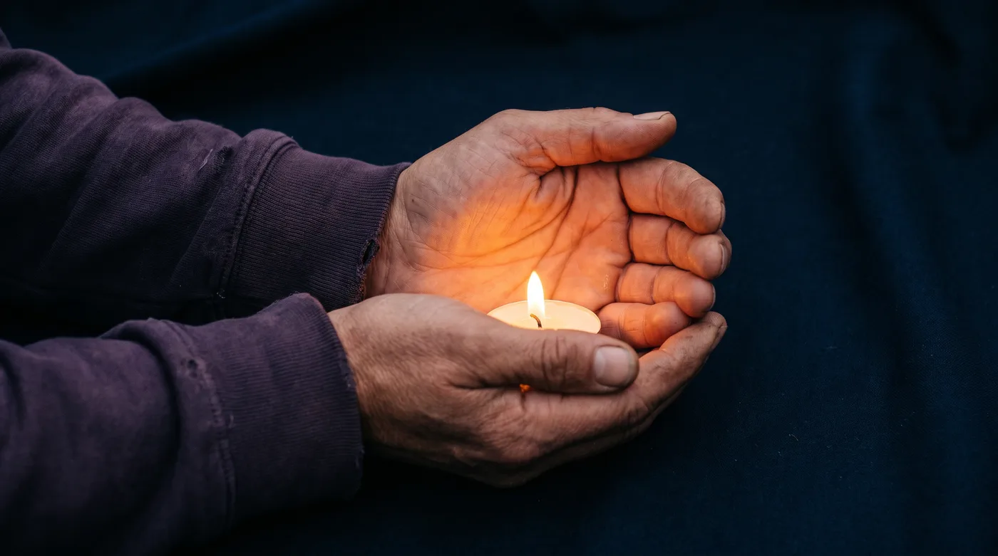 Two hands cupped around a single lit candle in the dark, honoring Maricopa County domestic violence victims